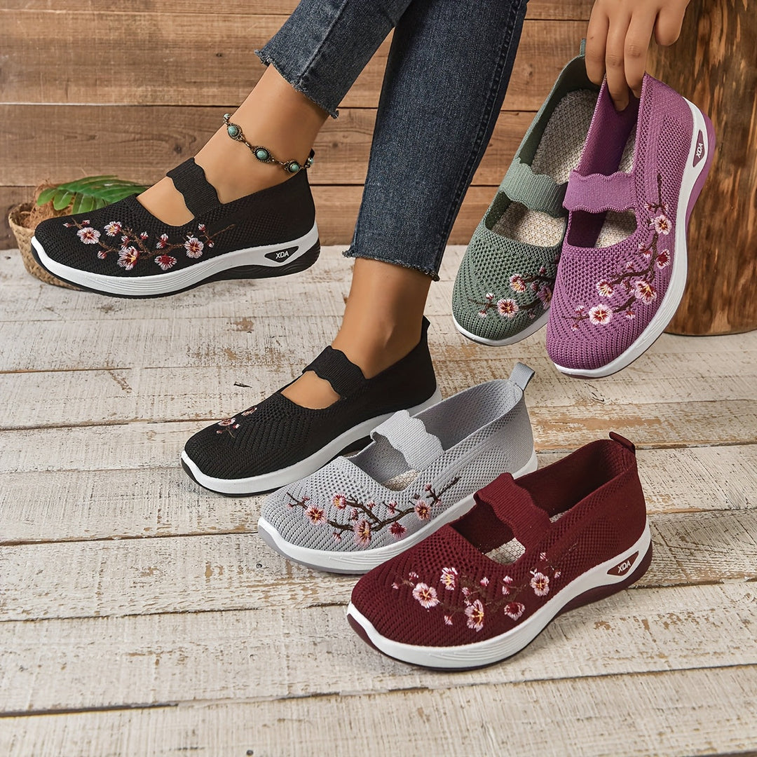 Damen-Sneaker mit Blumenstickerei in Schwarz, Grau, Lila und Rot auf Holzboden. Bequeme, modische Schuhe für Freizeit und Alltag.