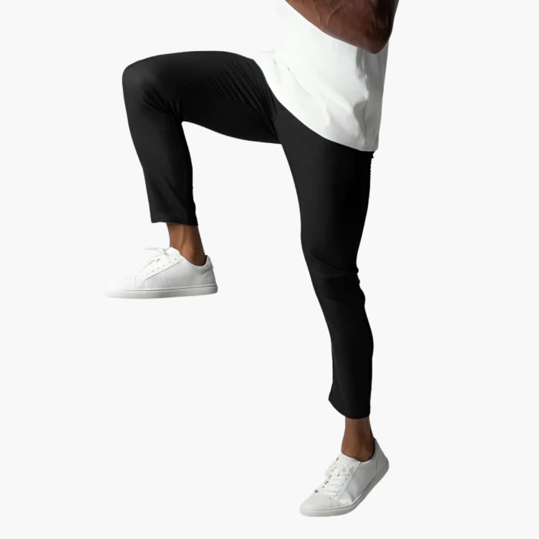 Mann in schwarzer Hose und weißen Sneakers hebt Bein, isoliert auf weißem Hintergrund. Mode, Herrenbekleidung, sportlicher Look.