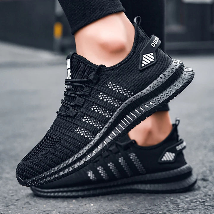 Schwarze Sportschuhe mit atmungsaktivem Mesh-Obermaterial und rutschfester Sohle, ideal für Laufen und Fitness, auf Asphalt getragen.