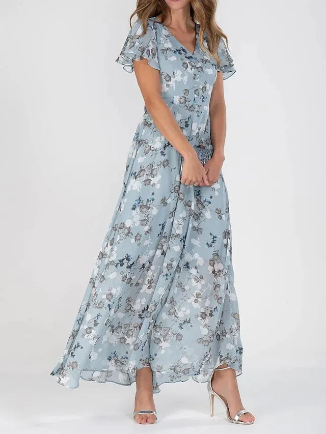 Frau in langem, blumigem Maxikleid in Blau mit V-Ausschnitt und kurzen Ärmeln, trägt silberne High Heels. Elegantes Sommeroutfit.