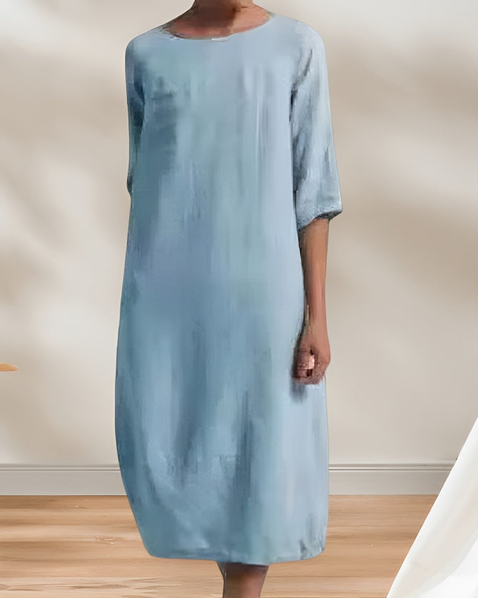 Frau in hellblauem, knielangem Kleid, stehend in minimalistischem Raum mit Holzboden. Elegantes, schlichtes Design, Mode, Damenbekleidung.