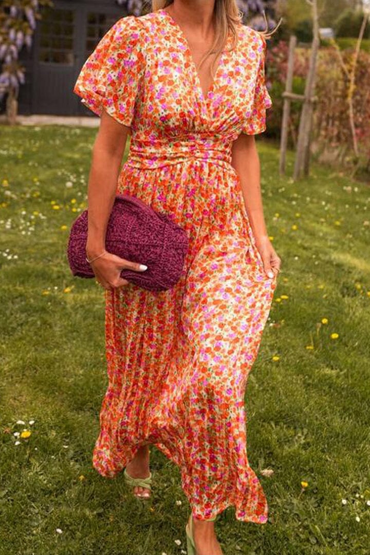 Frau in geblümtem Maxikleid mit lila Stricktasche auf grünem Rasen. Sommermode, florales Design, eleganter Look.