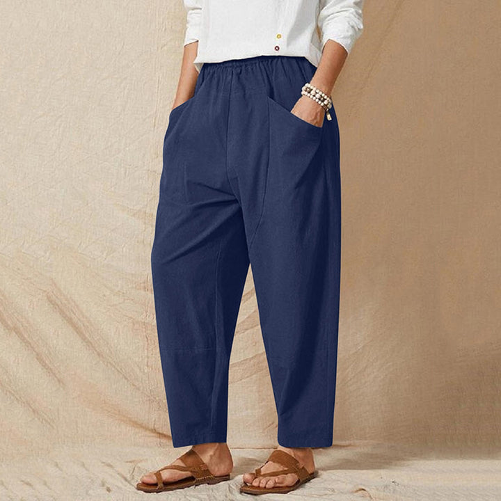 Person in blauer Leinenhose und weißem Oberteil, trägt Sandalen. Lässige Damenmode, bequeme Sommerkleidung, entspannter Stil.