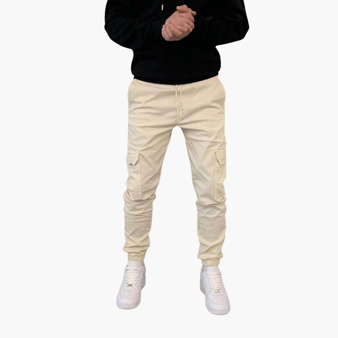 Mann in beiger Cargohose und weißen Sneakers, schwarzer Hoodie, Hände gefaltet. Modetrend, lässiger Stil, Herrenbekleidung.