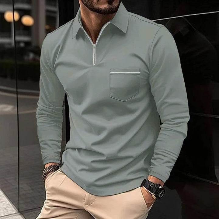 Mann in grauem Langarmshirt mit Reißverschluss und Brusttasche, beige Hose, Armbanduhr, städtische Kulisse. Herrenmode, Freizeitlook.