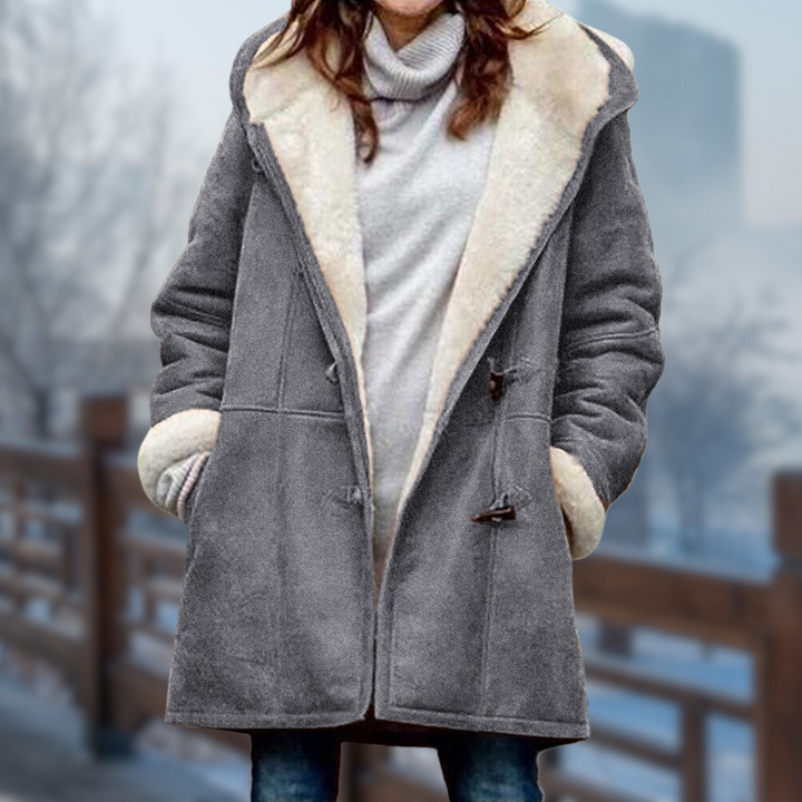 Frau in grauem Wintermantel mit weißem Fellkragen, stehend auf einer Brücke im Winter. Modischer Damenmantel, warm, stilvoll, Wintermode.