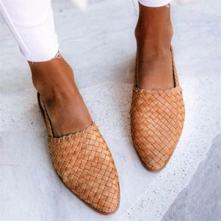 Geflochtene Damen-Slipper aus Leder in Beige, getragen mit weißen Jeans. Modische Sommerschuhe, bequem und stilvoll für Freizeit und Alltag.