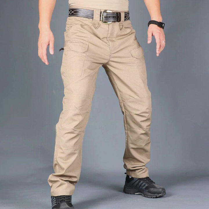 Beige taktische Hose für Herren, robustes Design, mit Taschen, schwarzer Gürtel und Schuhe, ideal für Outdoor-Aktivitäten und Abenteuer.