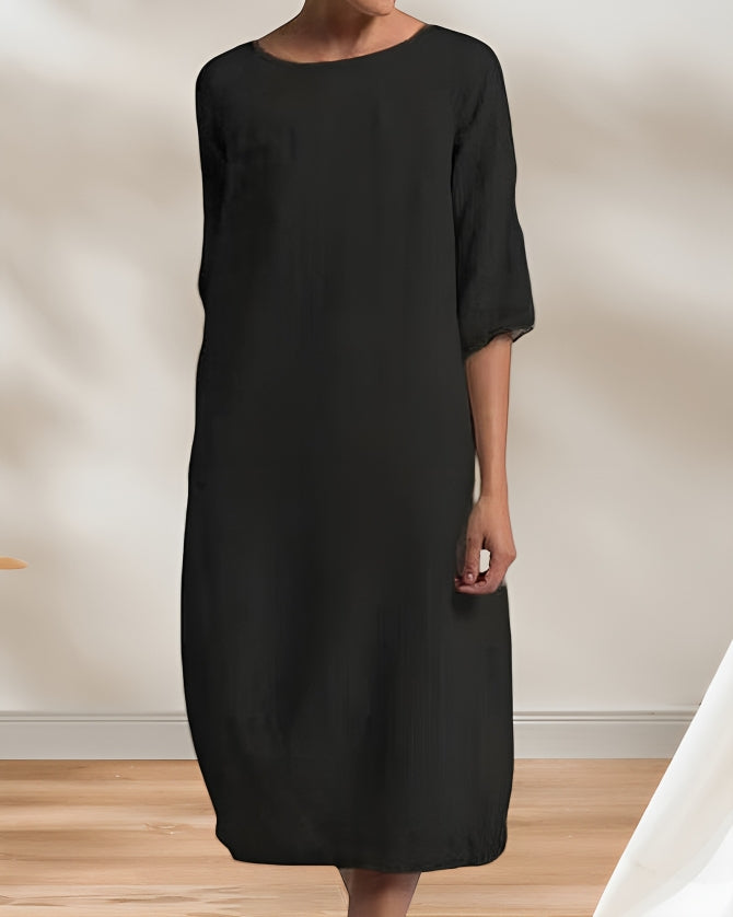 Frau in elegantem, schwarzem Kleid steht in minimalistischem Raum. Mode, Damenbekleidung, zeitloses Design, schlichte Eleganz, schwarzes Kleid.