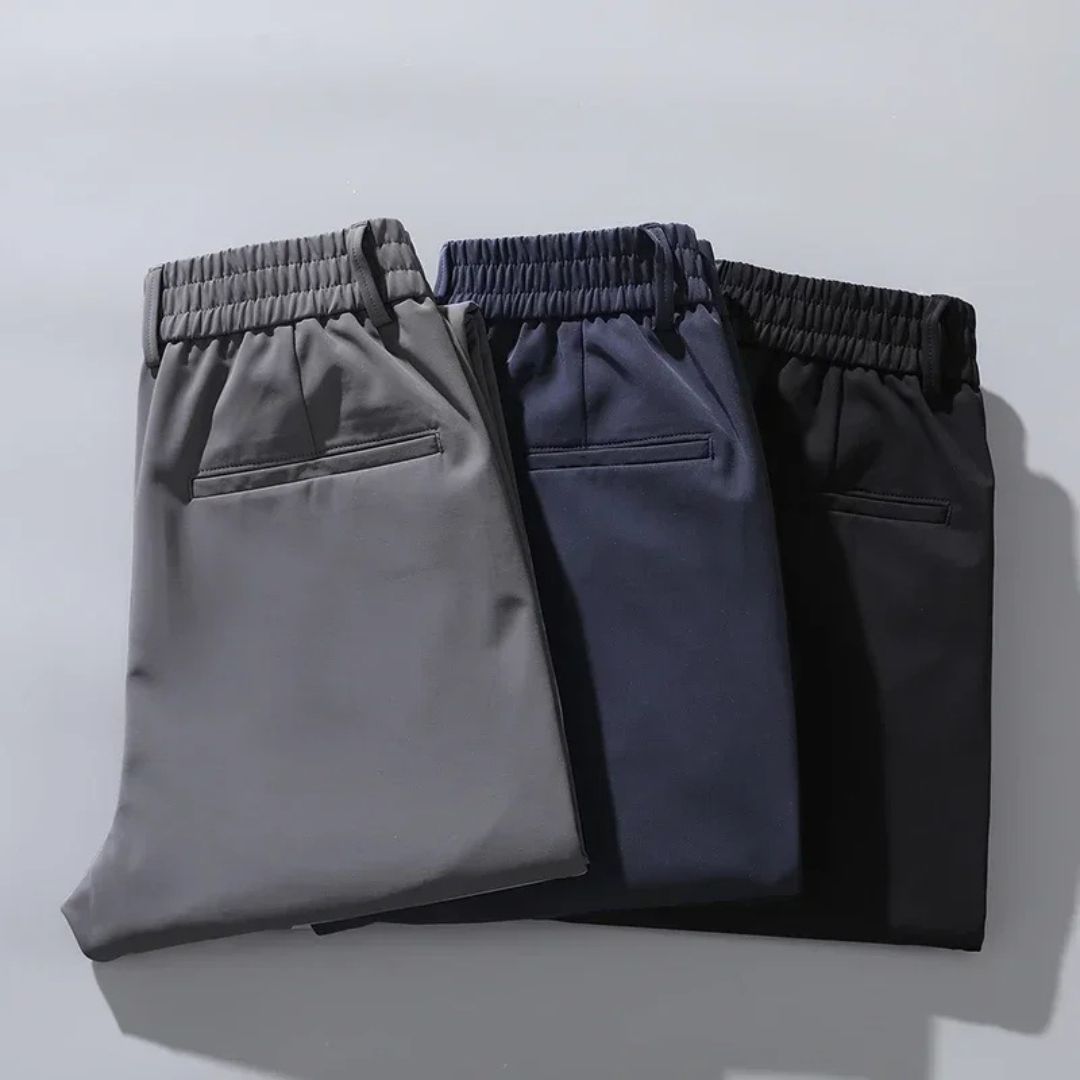 Drei gefaltete Herren-Chinohosen in Grau, Blau und Schwarz auf grauem Hintergrund. Bequeme, stilvolle Hosen für Freizeit und Büro.