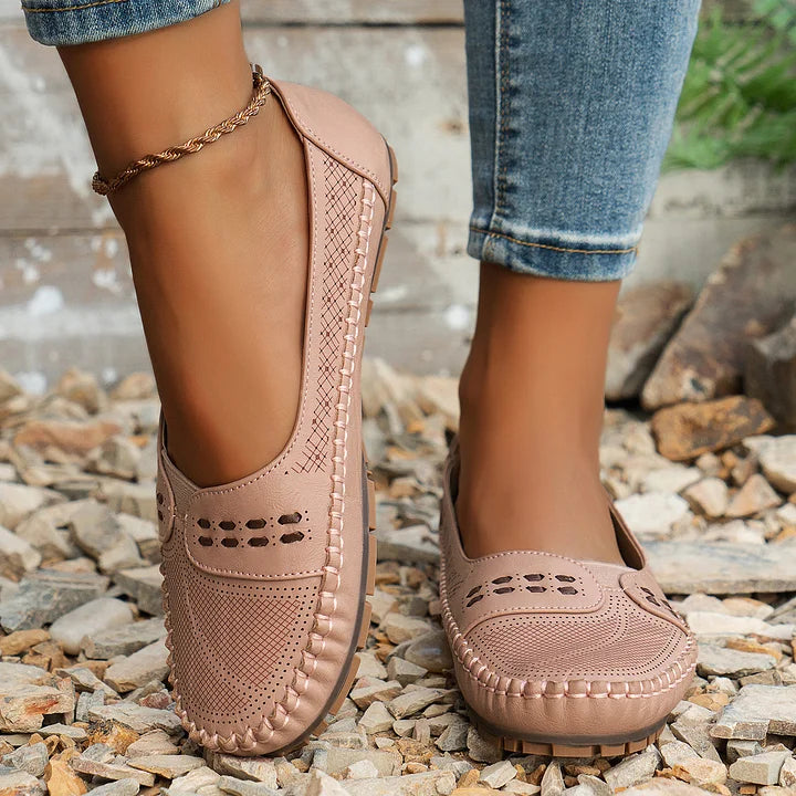 Damen Mokassins in Beige auf Kieselsteinen, mit Lochmuster und geflochtenen Details, kombiniert mit blauer Jeans. Bequeme Freizeitschuhe für den Sommer.