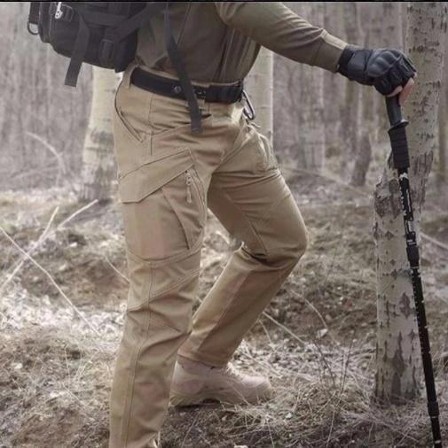 Person in Outdoor-Kleidung mit taktischer Hose und Wanderstock im Wald. Wandern, Outdoor-Abenteuer, Trekking-Ausrüstung, Naturerlebnis.