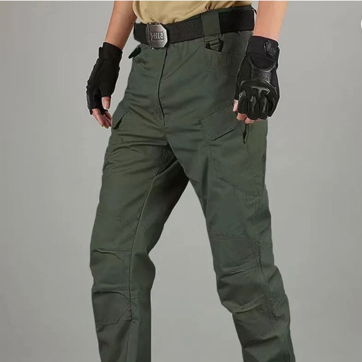 Person in taktischer Hose und Handschuhen, bereit für Outdoor-Aktivitäten. Robuste, grüne Hose mit mehreren Taschen, ideal für Abenteuer und Wandern.