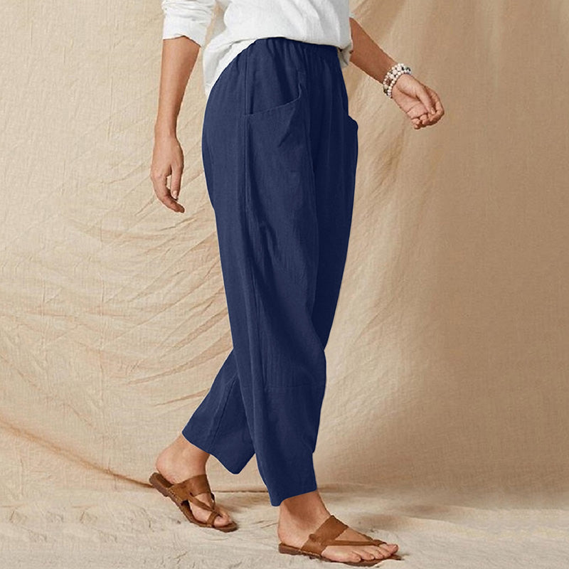 Frau in blauer Leinenhose und weißen Oberteil, trägt braune Sandalen. Lässige Mode, bequeme Sommerkleidung, stilvolle Damenbekleidung.
