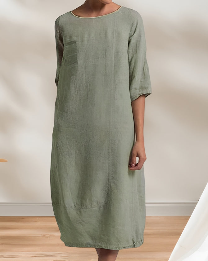 Frau in lockerem, knielangem, olivgrünem Leinenkleid mit 3/4-Ärmeln vor neutralem Hintergrund. Elegante, minimalistische Mode.