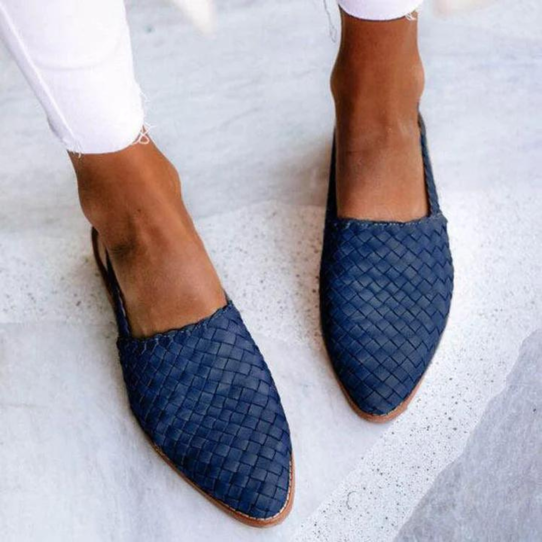 Damenfüße in blauen, geflochtenen Lederslippern auf hellem Boden. Modische Sommerschuhe, bequem und stilvoll, ideal für Freizeitoutfits.