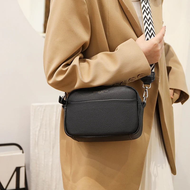 Damenhandtasche aus schwarzem Leder mit verstellbarem Schulterriemen, getragen von Person im beigen Blazer. Modische Umhängetasche für Alltag.