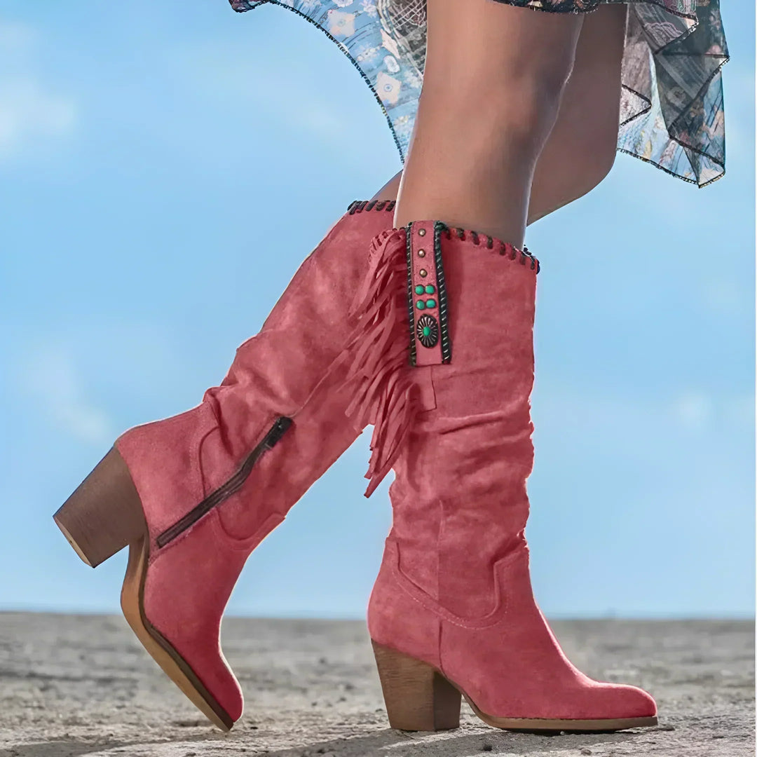 Rosa Cowboystiefel mit Fransen und Absatz, getragen von einer Person im Kleid. Modische Damenstiefel, ideal für Western- und Boho-Looks.