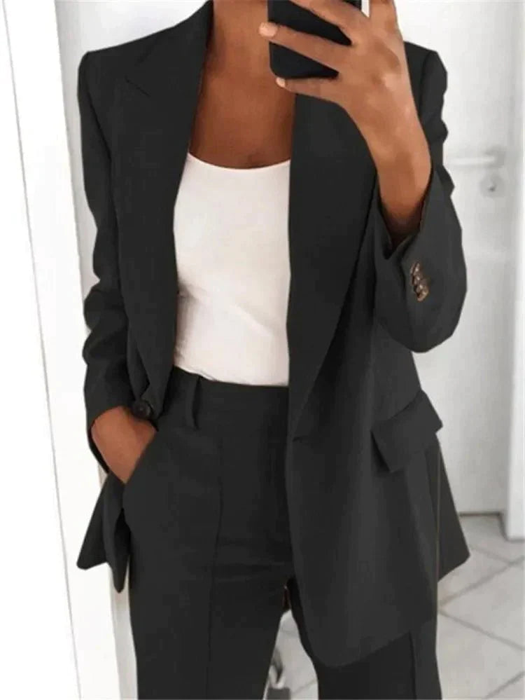 Frau in schwarzem Anzug und weißem Top macht Selfie; Businessmode, eleganter Blazer, professionelle Kleidung, modischer Look.