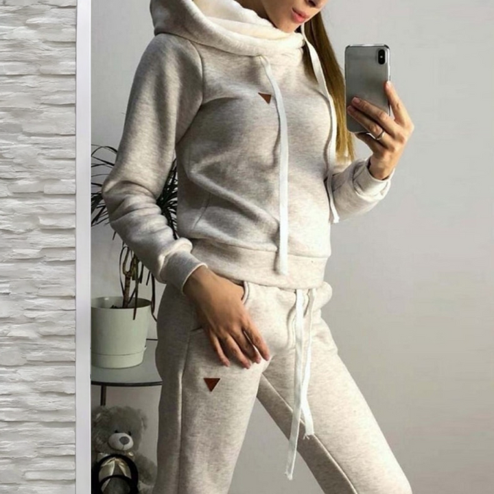 Frau in grauem Jogginganzug macht Selfie; gemütliche Sportbekleidung, Kapuzenpullover, Jogginghose, Freizeitmode, Indoor-Fitness-Outfit.