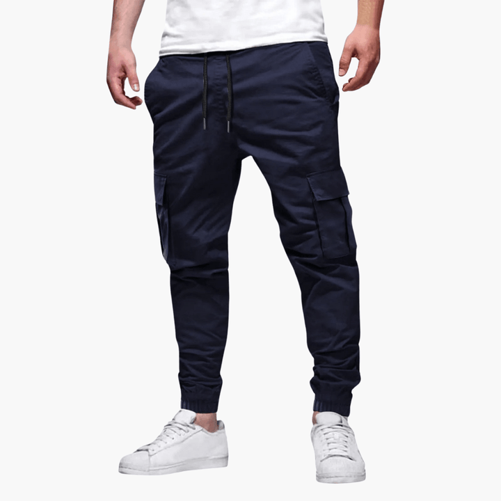 Dunkelblaue Cargo-Jogginghose für Herren, mit Seitentaschen und Kordelzug, kombiniert mit weißen Sneakers. Bequeme Freizeitmode.