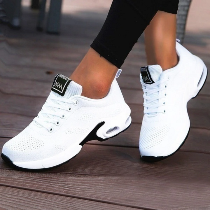Weiße Damen-Sneaker mit Luftpolstersohle auf Holzterrasse. Bequeme Sportschuhe, ideal für Laufen und Freizeit. Trendige, atmungsaktive Turnschuhe.