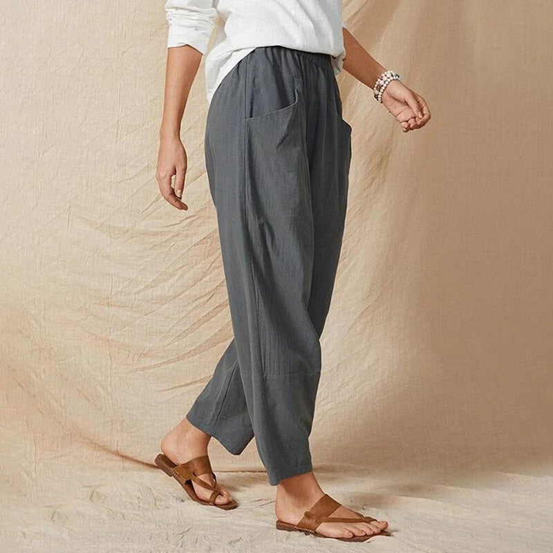 Frau in grauer Leinenhose und weißem Oberteil, trägt braune Sandalen. Modetrend, lässiger Stil, bequeme Damenbekleidung.