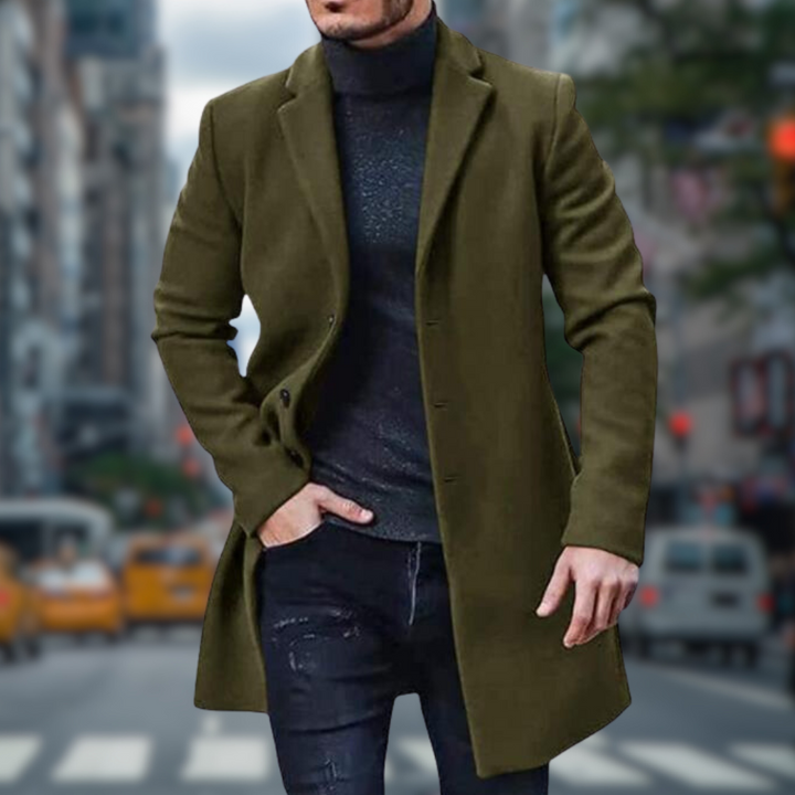 Mann in olivgrünem Mantel und schwarzem Rollkragenpullover auf belebter Stadtstraße mit gelben Taxis im Hintergrund. Elegante Herrenmode.