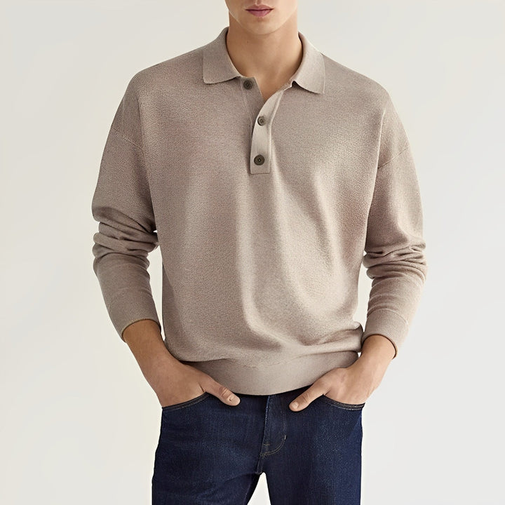 Junger Mann trägt beigen Pullover mit Knopfleiste und blaue Jeans. Modischer Freizeitlook, ideal für Herbstmode. Eleganter Herrenstil.