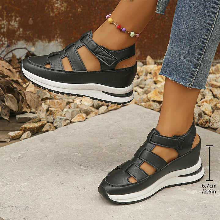 Frau trägt schwarze Plateau-Sandalen mit Klettverschluss, kombiniert mit Jeans. Modische Damen-Schuhe, ideal für Sommer und Freizeit.
