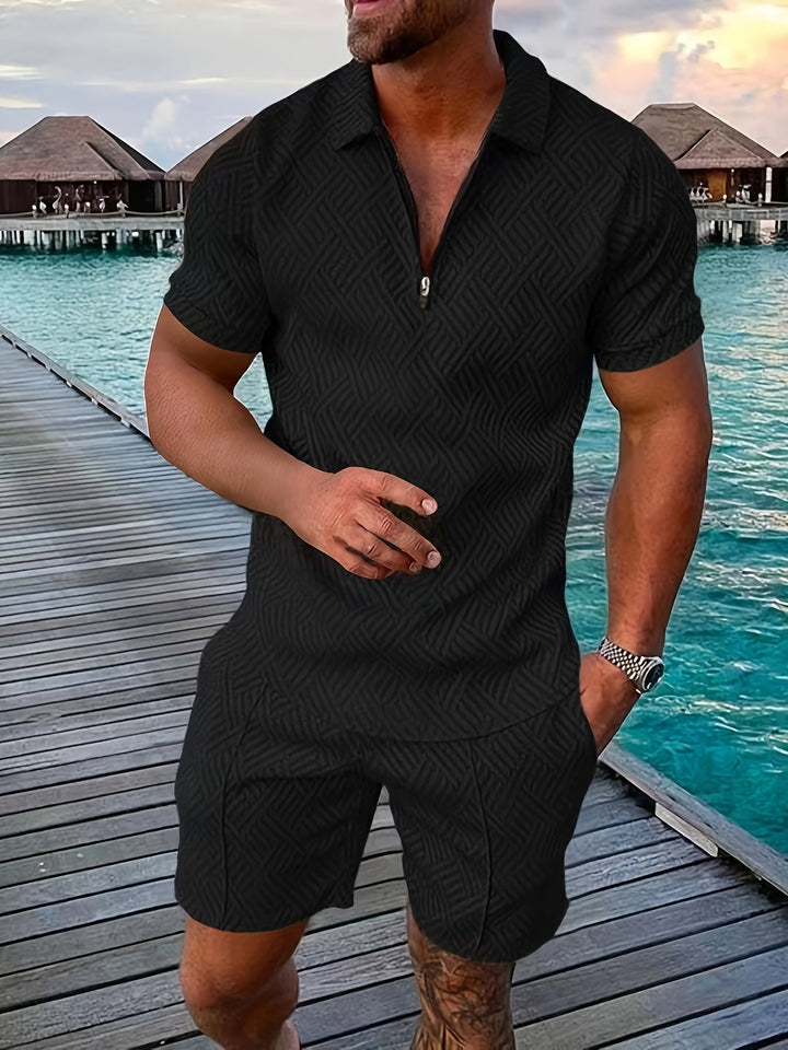 Mann in schwarzem, gemustertem Sommeranzug auf Holzsteg am Meer, im Hintergrund Wasserbungalows und blauer Himmel. Ideal für Urlaubs- und Sommermode.