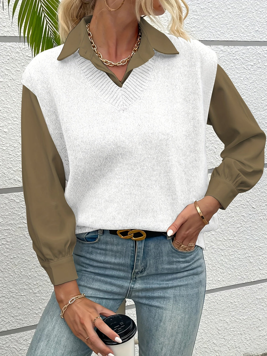 Frau in modischem Outfit mit weißem Strickpullover, olivgrüner Bluse, blauer Jeans und goldenen Accessoires, hält Kaffeebecher. Trendige Herbstmode.