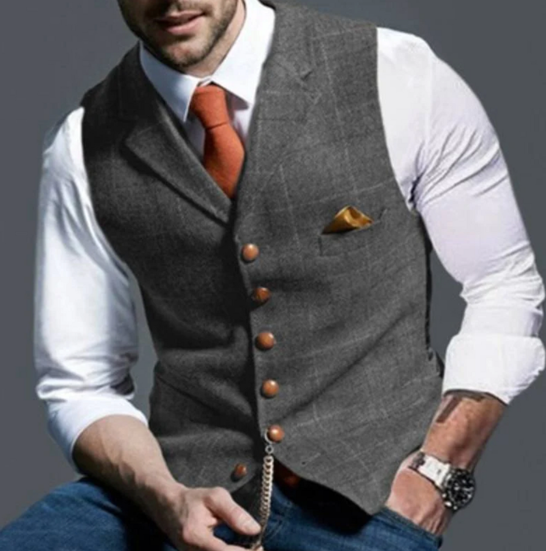 Mann in grauer Weste mit weißem Hemd und orangefarbener Krawatte, trägt Armbanduhr und Einstecktuch. Elegante Herrenmode, stilvoll gekleidet.