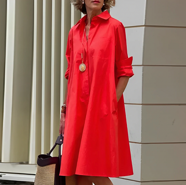 Frau in rotem Hemdkleid mit langen Ärmeln, trägt eine goldene Halskette und hält eine schwarze Tasche. Moderne Mode, eleganter Stil, Stadtumgebung.