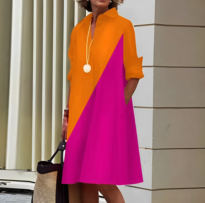 Frau in farbenfrohem Kleid mit orange-pinkem Design, steht vor moderner Architektur. Modetrend, Sommerkleid, stilvolle Damenmode.