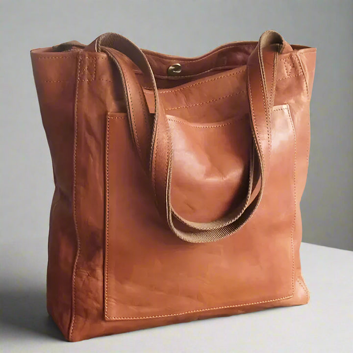 Braune Ledertasche mit zwei Henkeln auf grauem Hintergrund. Stilvolle, geräumige Handtasche für Damen. Ideal für Alltag und Büro.