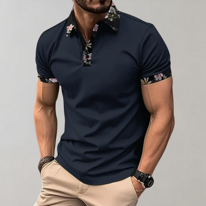 Dunkelblaues Herren-Poloshirt mit floralen Akzenten an Kragen und Ärmeln, kombiniert mit beigen Hosen. Modischer Freizeitlook für Männer.