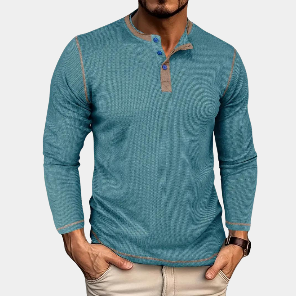 Mann trägt blaues Langarm-Henley-Shirt mit Knopfleiste, kombiniert mit beigen Hosen. Modischer Freizeitlook für Herrenmode.
