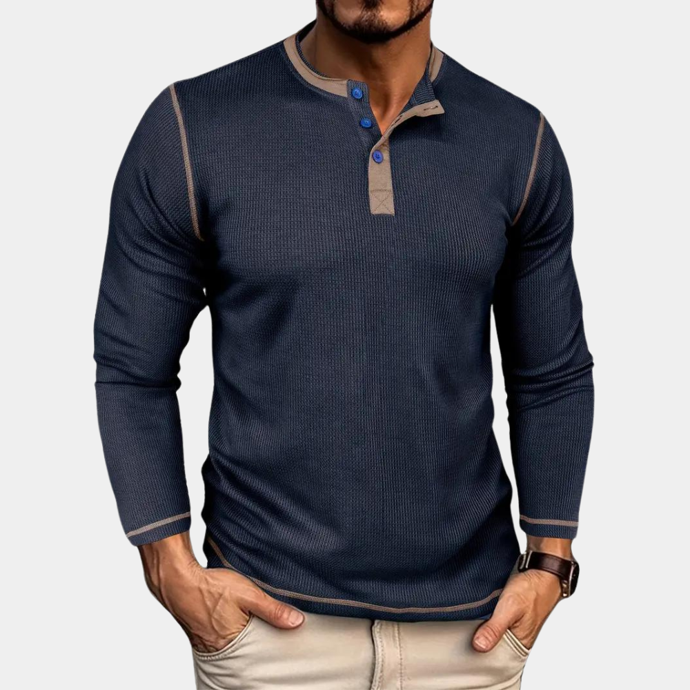 Mann trägt dunkelblaues Langarmshirt mit Knopfleiste, kombiniert mit beigen Hosen. Modischer Herrenstil, lässiges Outfit, Herbstmode.
