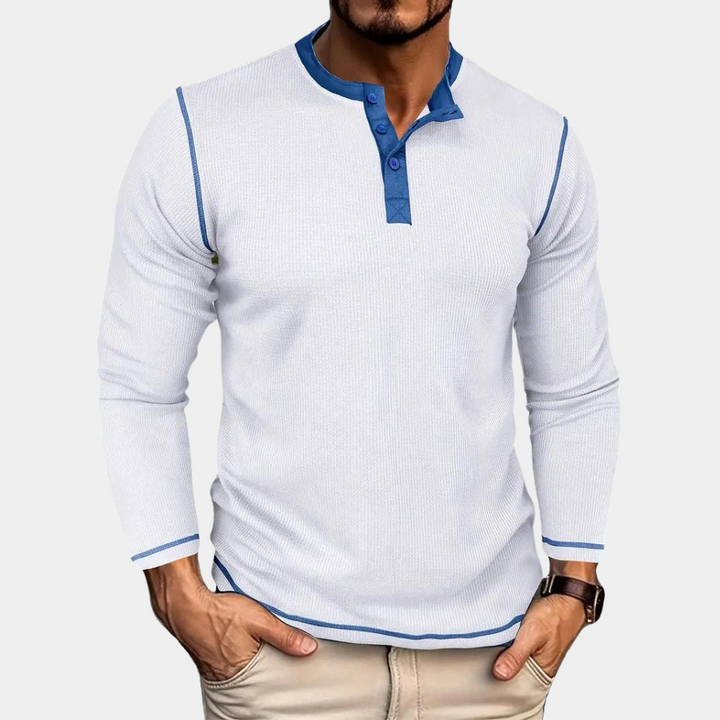 Mann trägt weißes Langarmshirt mit blauen Akzenten und Knopfleiste, kombiniert mit beigen Hosen. Modische Herrenbekleidung, Freizeitlook.