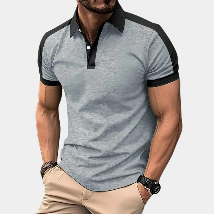 Mann trägt graues Polohemd mit schwarzen Akzenten, kombiniert mit beigen Hosen. Modisches Herrenoutfit, lässiger Stil, Sommermode.