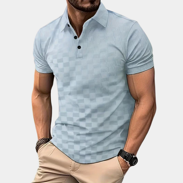Mann trägt hellblaues kariertes Poloshirt mit kurzen Ärmeln, kombiniert mit beigen Hosen. Modischer Freizeitlook, ideal für Sommermode.