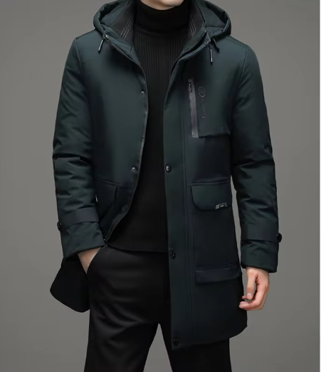 Dunkelgrüner Herrenmantel mit Kapuze, Reißverschlusstasche und Knöpfen, getragen über einem schwarzen Rollkragenpullover. Elegante Wintermode.