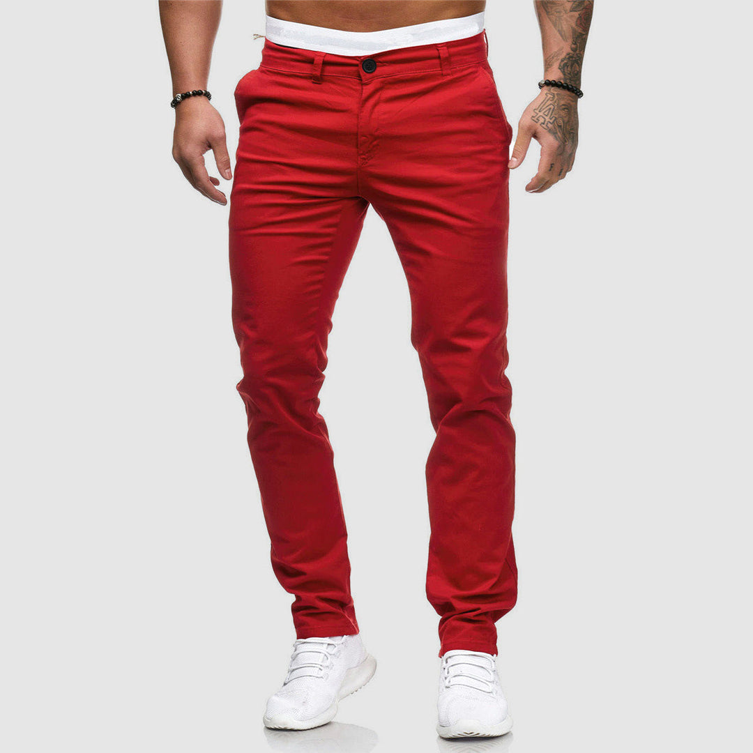 Mann in roten Chinos und weißen Sneakers vor grauem Hintergrund. Modische Herrenbekleidung, lässiger Stil, trendige rote Hose.