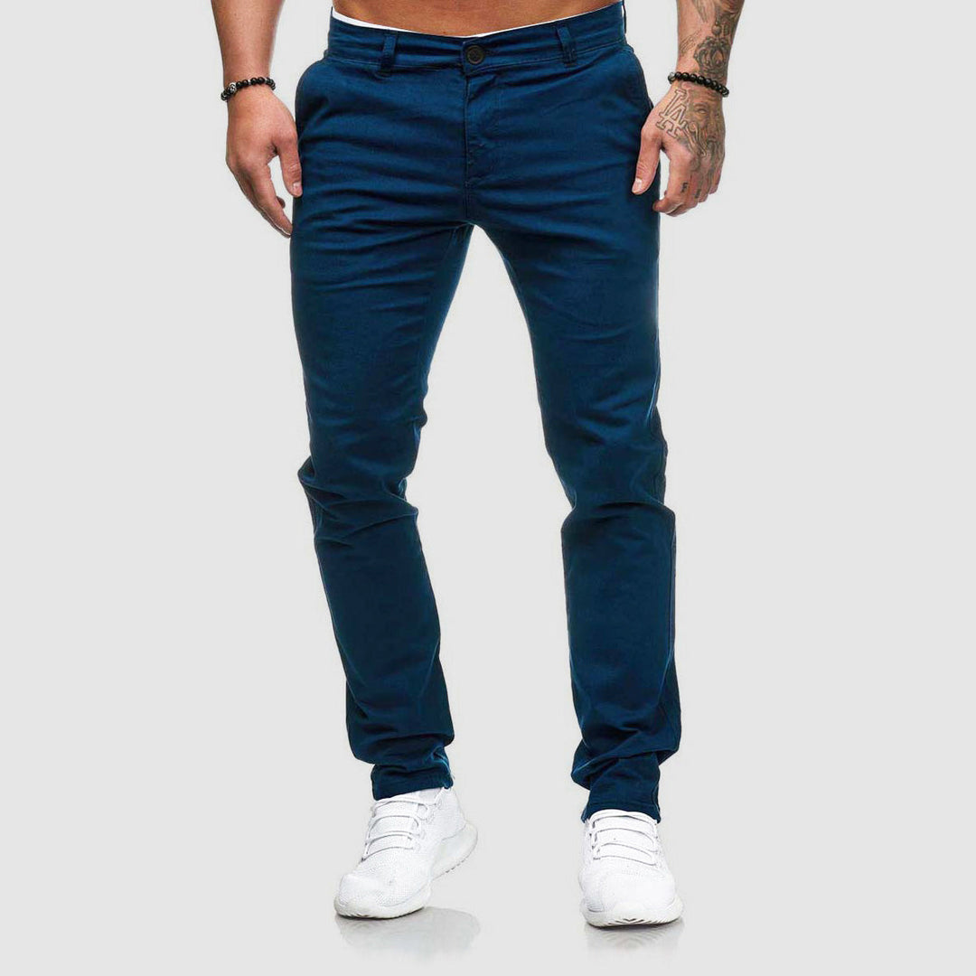 Mann trägt dunkelblaue Chinohose und weiße Sneaker, isoliert auf grauem Hintergrund. Modische Herrenbekleidung, lässiger Stil.