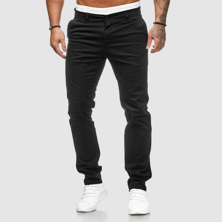 Mann in schwarzer Chinohose und weißen Sneakers vor grauem Hintergrund. Modische Herrenbekleidung, lässiger Stil, moderne Herrenmode.