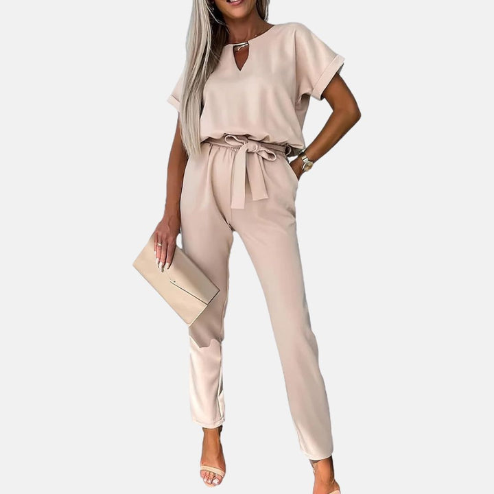 Eleganter Damen-Jumpsuit in Beige mit Gürtel, kombiniert mit Clutch und Sandalen. Perfekt für stilvolle Sommermode und Freizeitoutfits.