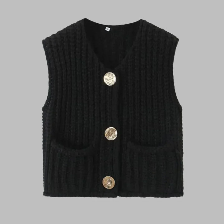 Schwarze Strickweste mit drei goldenen Knöpfen und zwei Taschen, ärmellos, auf grauem Hintergrund. Modische Damenbekleidung, Herbstmode.