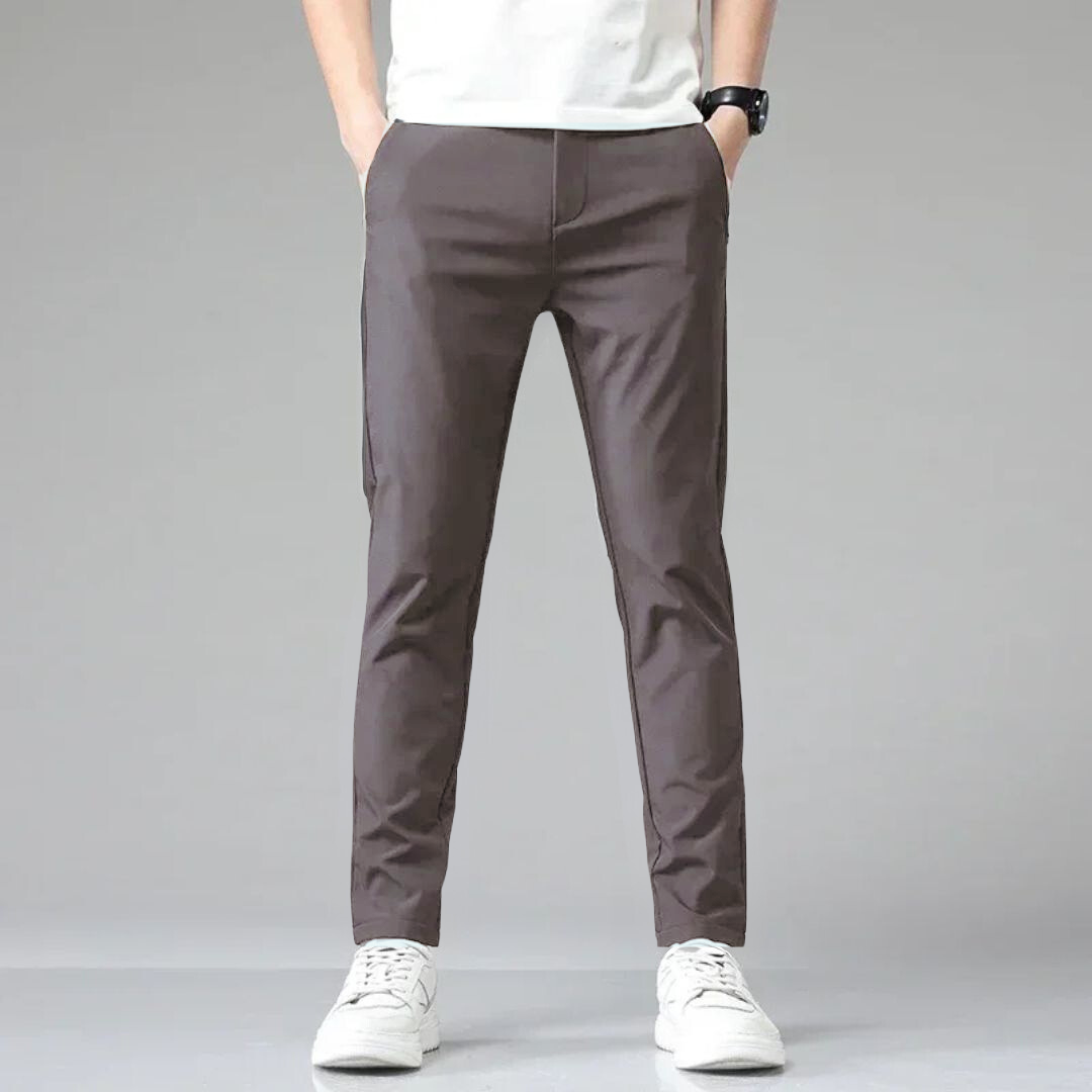 Mann trägt graue Chinohose, weißes T-Shirt und weiße Sneaker. Moderne Herrenmode, lässiger Stil, ideal für Freizeit und Alltag.