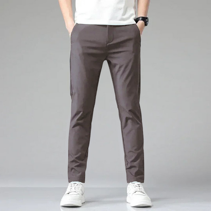 Mann trägt graue Chinohose, weißes T-Shirt und weiße Sneaker. Moderne Herrenmode, lässiger Stil, ideal für Freizeit und Alltag.